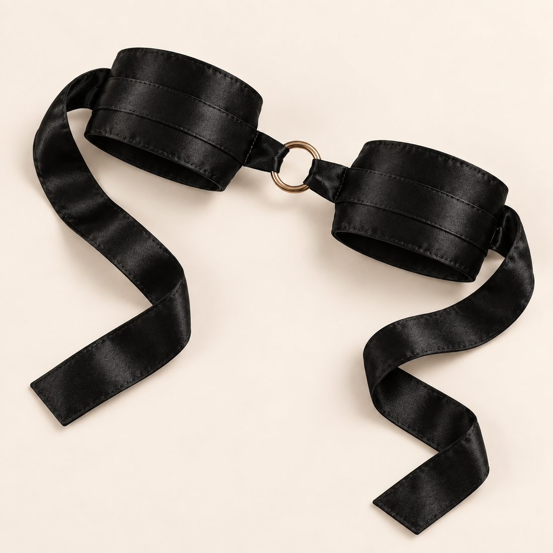 Pair of black satin wrist cuffs with tie ribbons and a connecting ring, shown flat on an ivory background